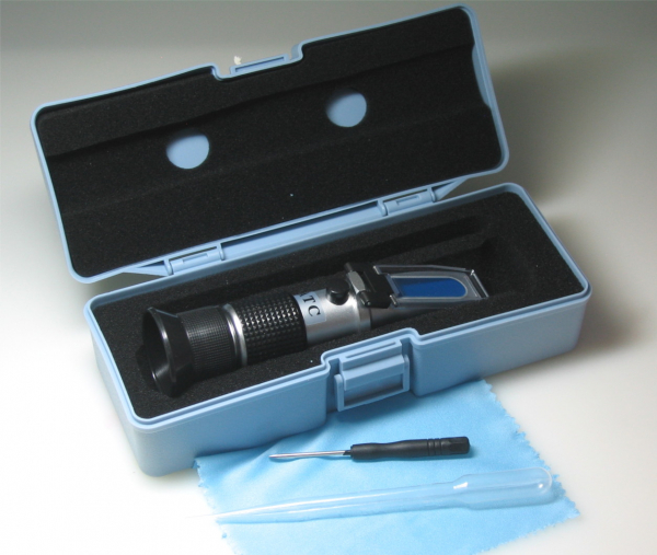 The picture shows a plastic box containing a refractometer, a screwdriver, a pipette, and a cleaning cloth.